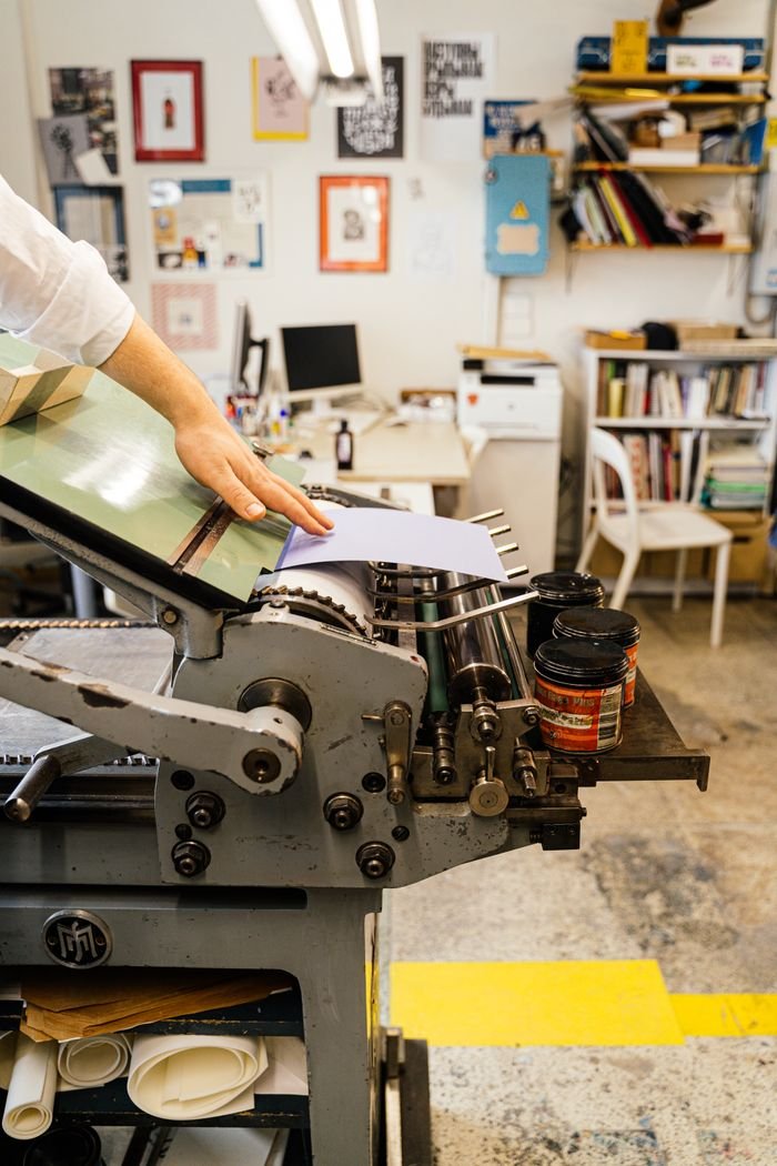 Close-up of a hand operating a vintage printing press inside an artisan workshop.